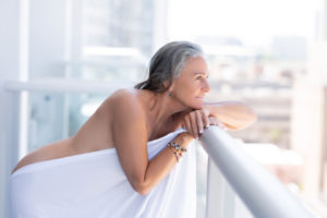 Mature woman posing on a balcony covered by a white sheet for a boudoir photoshoot