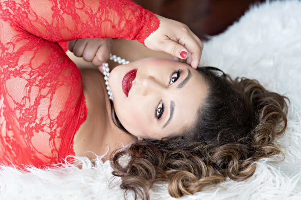 Curvy woman wearing a red lace long sleeve and red lipstick posing for boudoir portrait