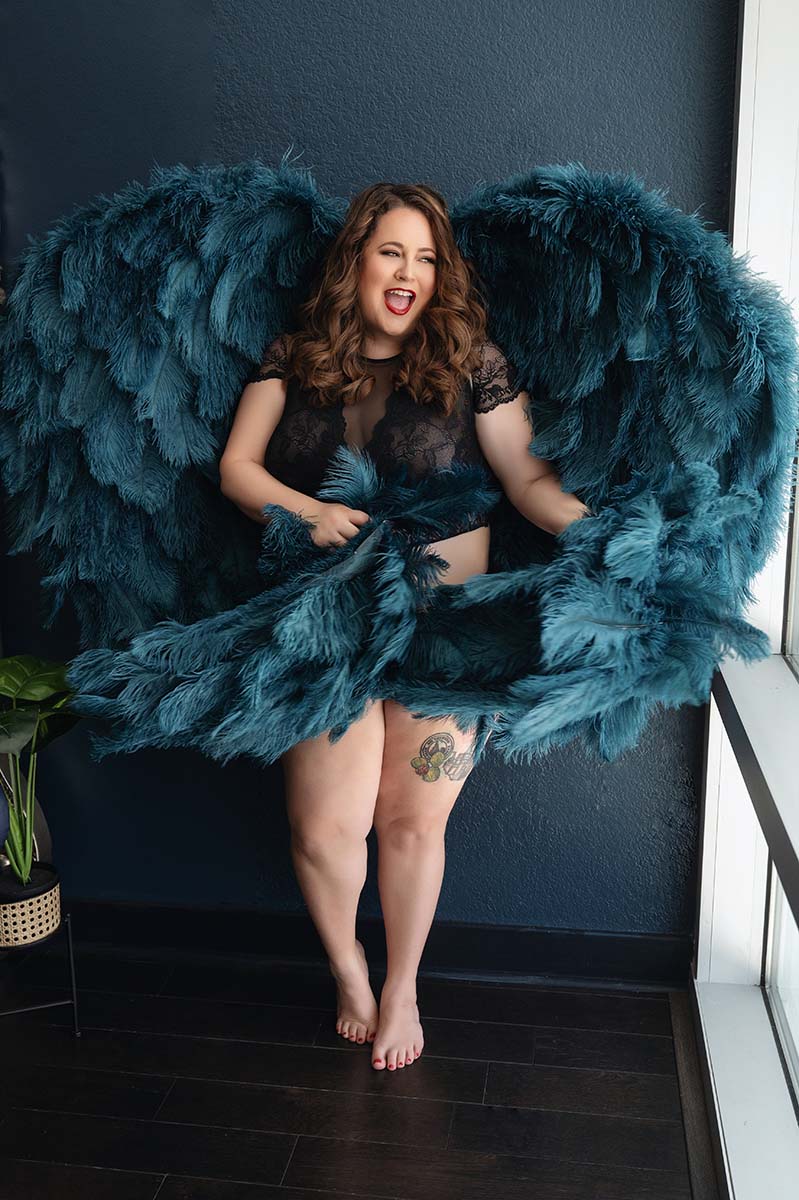 Portrait of curvy woman posed laughing holding the tips of teal wings