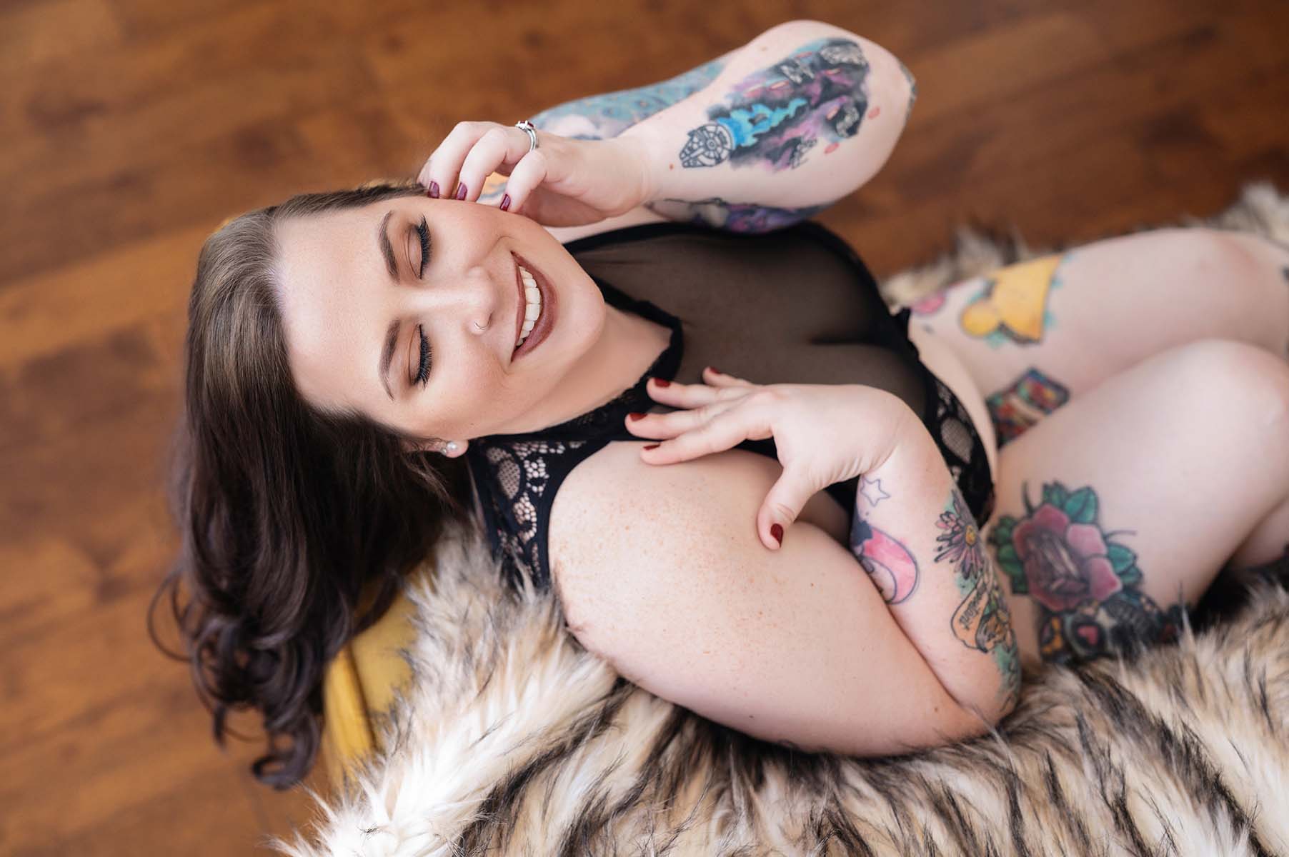 Tattooed woman posing for a boudoir portrait laying against yellow couch covered by beige fur blanket