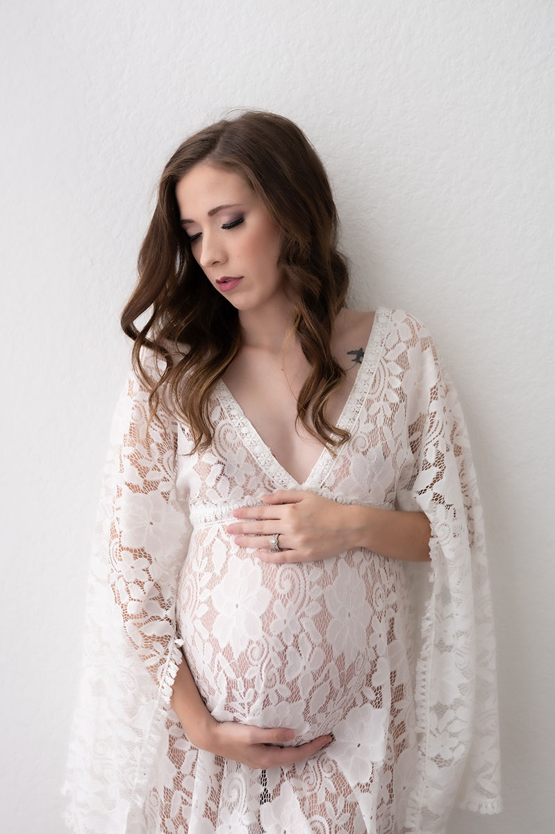 Brunette woman posing for maternity portrait wearing a long sleeve lace dress